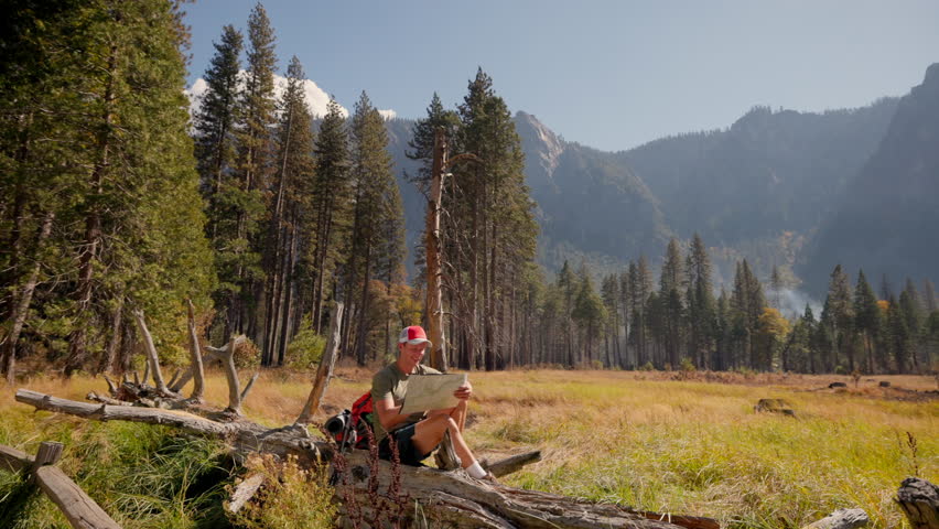 Dedicated hiker studies a map in breathtaking Yosemite National Park, surrounded by majestic mountains, towering trees, and vibrant wildernessthe perfect setting for a memorable camping adventure