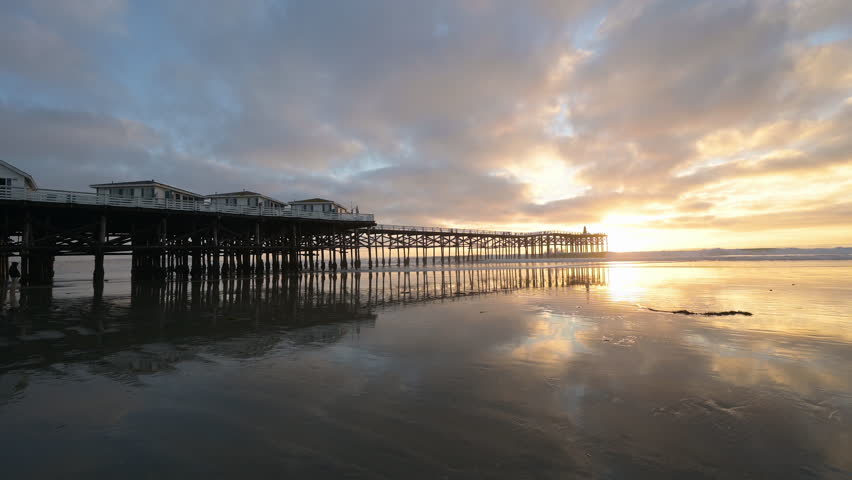 Crystal Pier Cottages Pacific Beach San Diego California sunset. Static shot. Silhouetted people walk into the frame from the right.