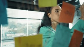 Portrait of smart professional hispanic businesswoman writes marketing ideas on glass board with colorful sticky notes. Young manager drawing mind map to analysis business plan. Closeup. Manipulator. - Powered by Shutterstock - Get 15% off with code: PIKWIZARD15