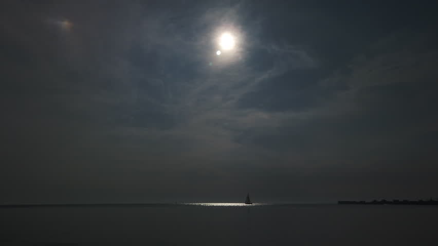 A sailboat in the distance moving slowly through a beam of sunlight on Lake Ontario