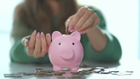 Woman saving cash in bank. Close up of woman placing coins into piggy bank. Concept of financial planning. Piggy bank symbolizes saving cash. Woman managing finances. Budgeting and financial security. - Powered by Shutterstock - Get 15% off with code: PIKWIZARD15