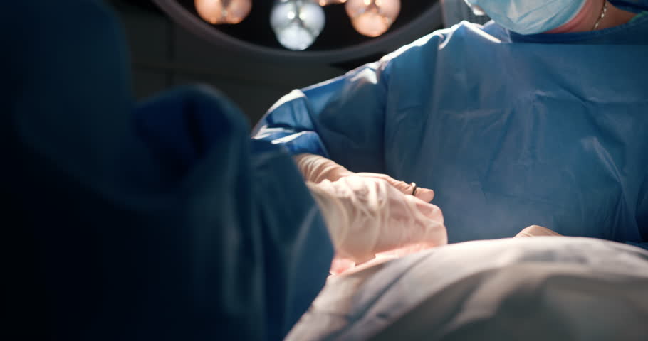 Surgeons with masks performing modern operation in hospital. Focus on precision, teamwork, sterile environment. Asian and Caucasian adult professionals engaged in surgical procedure under lights