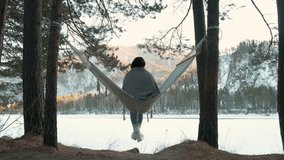 Winter landscape featuring young woman relaxing in hammock strung between pine trees, overlooking frozen lake during serene sunset with snow-covered surroundings - Powered by Shutterstock - Get 15% off with code: PIKWIZARD15