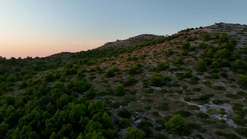 Rugged shrubs grow on rocky hills, sunset golden glow in Kornati, Croatia, across the sky and waters, drone ascend