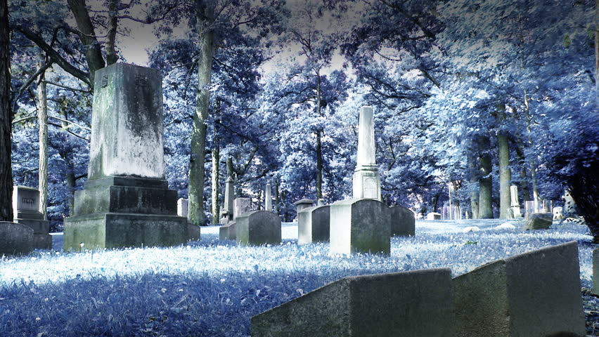 Various ghostly shapes pass through the tombstones in a deserted graveyard.