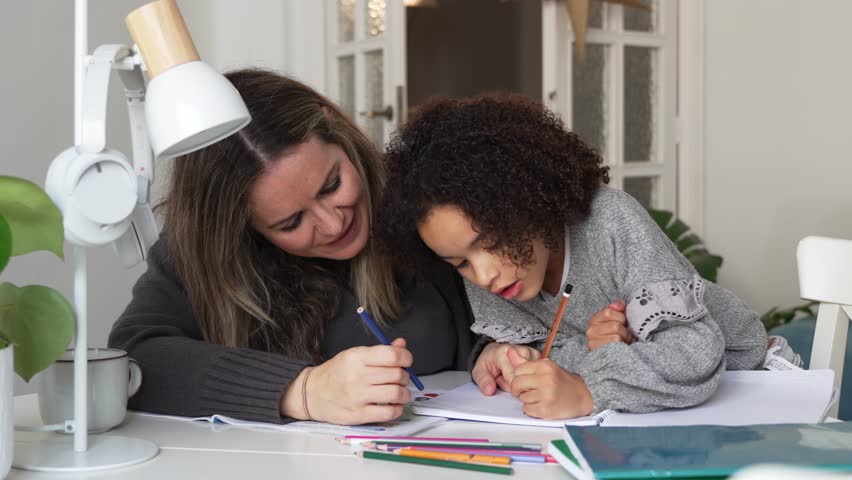 Caucasian mother and African American daughter studying at home, doing homework in cosy white room. Parent teach, child school girl learn knowledge, write exercise read book. Education for children