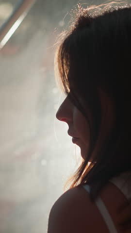 Sad woman silhouette near reflective glass closeup. Lady stands alone by window mirror surface at night. Woman with depression at backlight