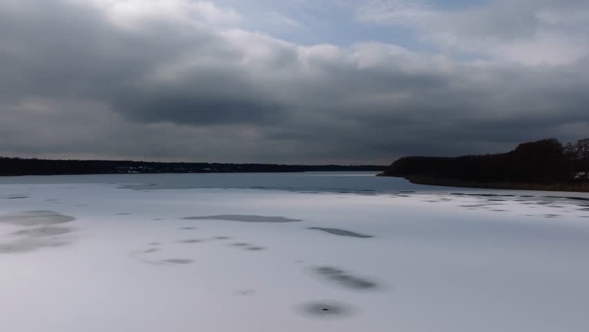 A drone landscape view of frozen waters under cloudy sky at sunset, and a dark horizon line in the background