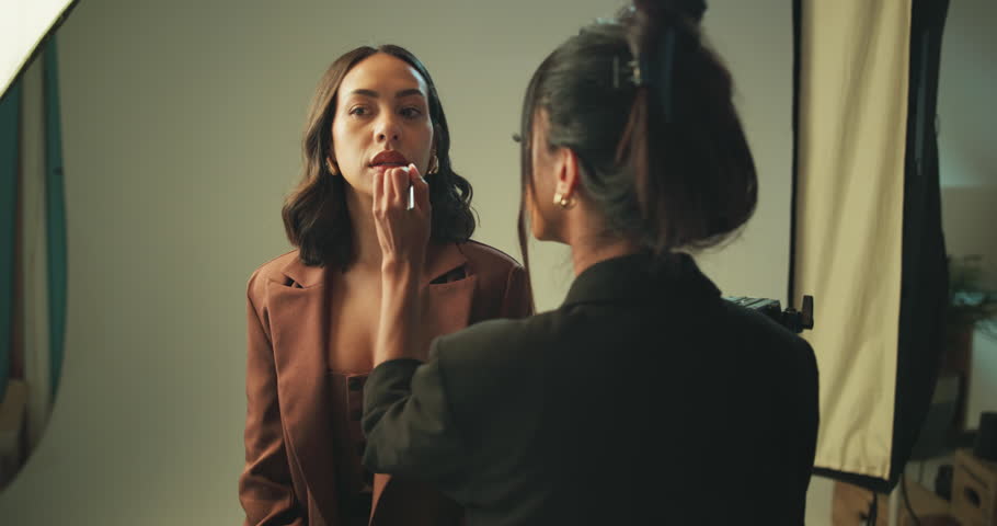 Studio, makeup artist and women with tools, lipstick and preparing for photoshoot, glow and cosmetics. Production, model and makeover with brush on set, behind the scenes and people with equipment