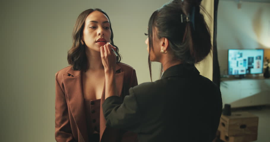 Studio, makeup artist and women with tools, lipstick and preparing for photoshoot, glow and cosmetics. Production, model and makeover with brush on set, behind the scenes and people with equipment