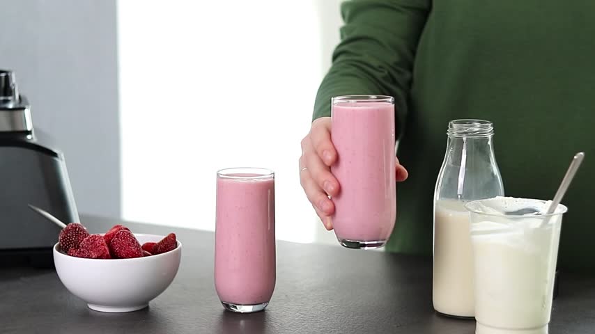 Close up of a woman in green sweater preparing fresh strawberries smoothie with yogurt and milk in the kitchen 