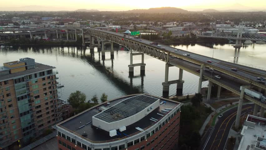 Traffic on Marquam Bridge crossing Willamette River during golden sunrise. Aerial forward wide shot. Light behind mountains in suburb. Portland, Oregon, USA.