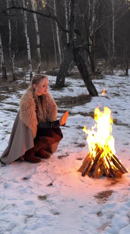 Beautiful blonde girl with hairstyle in fur medieval dress  posing at night near bonfire. Fairy tale story about warrior . Warm art work.