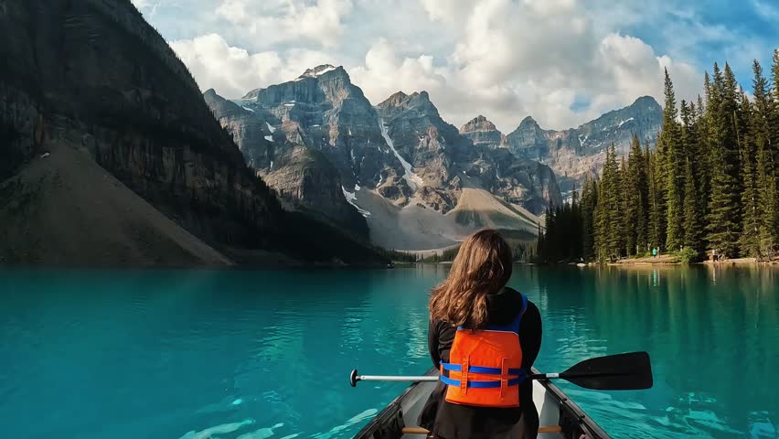A  back shot of a woman paddles through the crystal-clear waters of Moraine Lake, Alberta, Canada