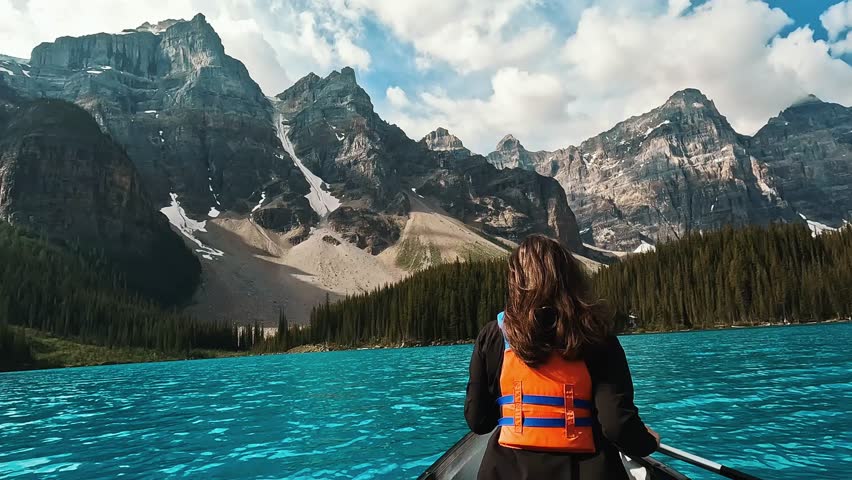A  back shot of a woman paddles through the crystal-clear waters of Moraine Lake, Alberta, Canada