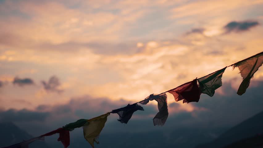 4K Slow motion shot of prayer flags waving in the wind in front of snowy Himalayan mountain peaks covered by clouds during the sunset at Khangsar village in Lahaul valley, Himachal Pradesh, India.