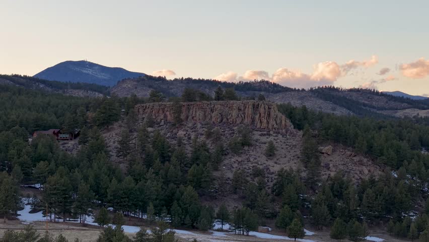 Aerial view of a rugged plateau surrounded by dense forest, with mountains in the background at sunset
