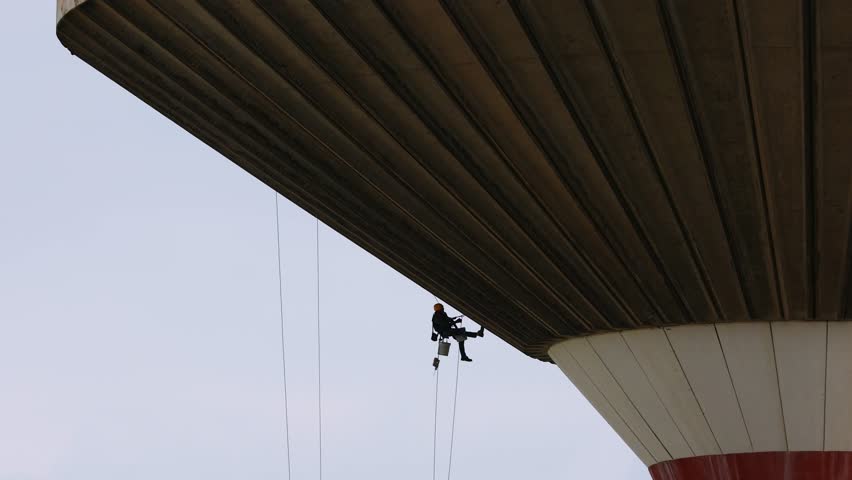 Acrobatic building worker performing restoration on an old brutalist aqueduct suspended by ropes with safety harness featuring industrial architecture construction techniques structural maintenance