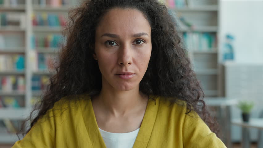 Serious confident Arabian Hispanic Latina woman library university college student female learning education teacher looking at camera calm sad upset girl portrait high school lady expression studying