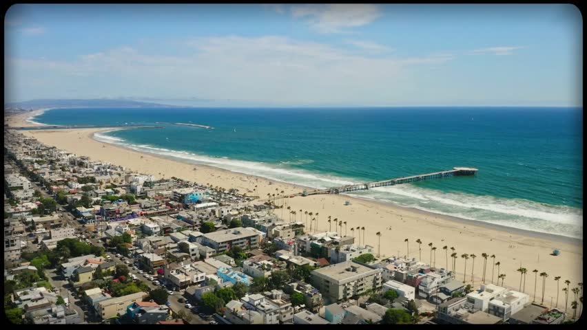 A stunning aerial view of a beautiful sandy beach with a long pier extending into the ocean. The coastline is lined with palm trees and buildings, capturing the essence of a perfect coastal vacation. 
