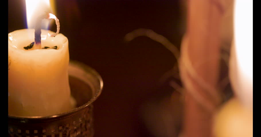 A macro shot from candle flames past the trickling sand of a medieval hourglass illuminated by the candlelight.