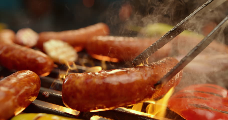 Extreme close-up view of an unrecognizable chef flipping sausages with tong, super slow-motion footage