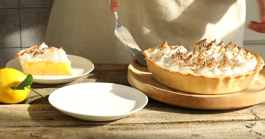 Woman serving piece of lemon meringue pie at wooden table, closeup
