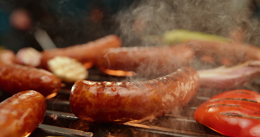 Super slow-motion close-up of sausages grilling on a black grill, flame coming out from the stove