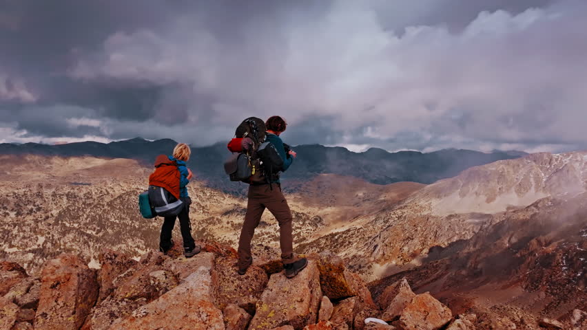 Adventure seekers stand on rocky peaks, soaking in stunning views of the Pyrenees mountains under a dramatic sky during their hike in Spain.