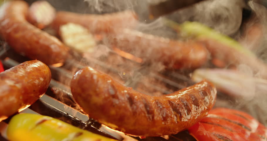 Extreme close-up view of a few sausages roasting on the fire grill with burning fire and smoke