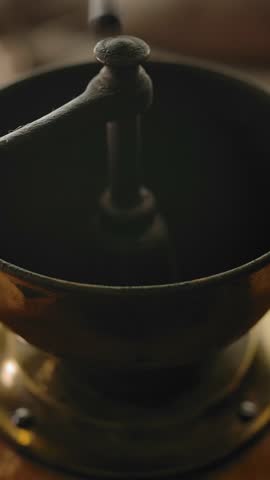 Dropping roasted coffee beans inside of coffee grinder for traditional coffee making in an authentic way. Slow motion close-up. Vertical shot.