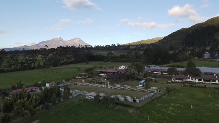 Scenic farm in the Ecuadorian Andes with a stable, cows, and a tractor on lush green pastures. A majestic snow-capped mountain in the background completes this stunning rural landscape