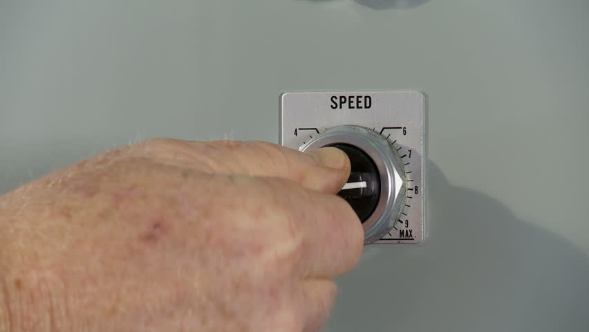 Hand adjusts a rotary dial, increasing the speed of a machine. Close up,