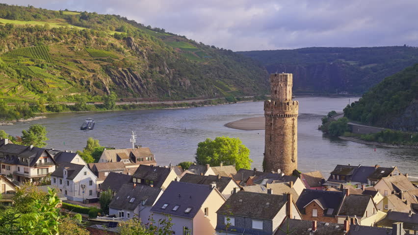 Morning sunrise over the Rhine River Valley with a small riverside town, Oberwesel, a Medieval Tower, Ochsenturm, and romantic rolling hills with vineyards, Germany