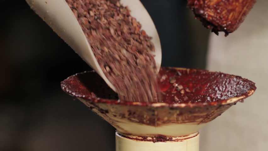 Four clips showing stages of broken up cocoa nibs being put through a juicer to