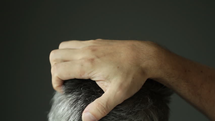 Man with grey hair scratching his head. Recorded with shallow depth of field.