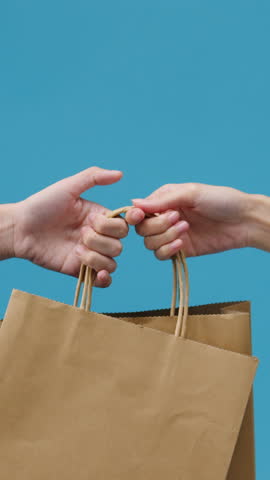 Vertical Screen : Young woman hand hold brown clear empty blank craft paper bag food for takeaway over blue background. Copy space for place text for advertisement. Advertising area, mock up content.