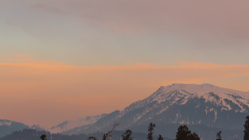 4K timelapse of sunset over snowy Himalayas during winter at Gulmarg, Jammu and Kashmir, India. Orange color clouds moving over mountains during evening. Sunset time lapse.