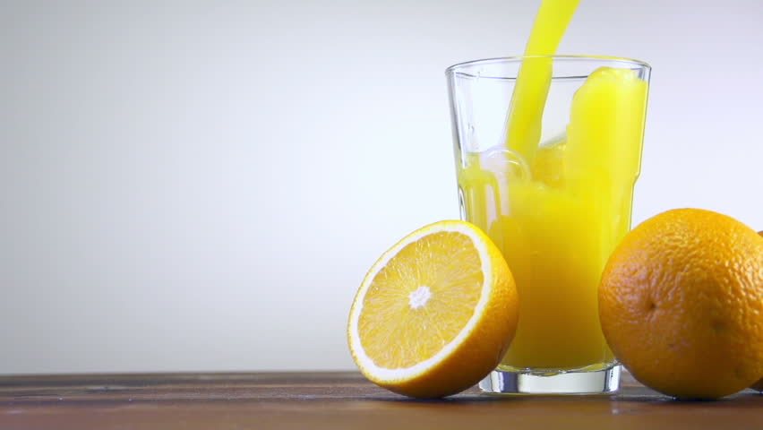 Orange juice pouring in glass on color background