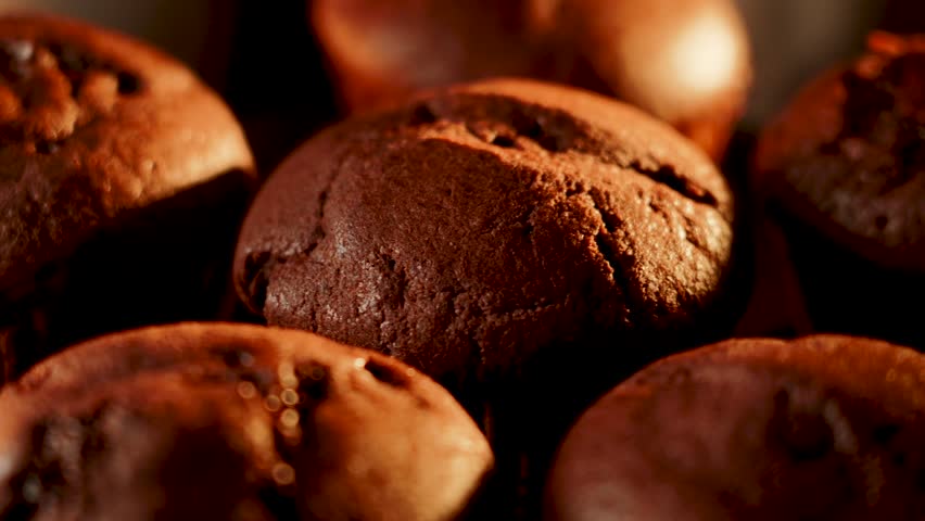 Chocolate muffins spin under warm light on a black background creating a tempting visual treat