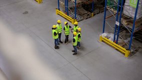 Warehouse workers wearing safety vests and helmets are gathering and discussing logistics and inventory management in a large distribution center, seen from a high angle view - Powered by Shutterstock - Get 15% off with code: PIKWIZARD15