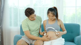 Beautiful pregnant wife with headphones enjoys listening to music for relaxation while husband take care of her, Mom and Dad feeling happy smiling peaceful while take care baby in the womb - Powered by Shutterstock - Get 15% off with code: PIKWIZARD15
