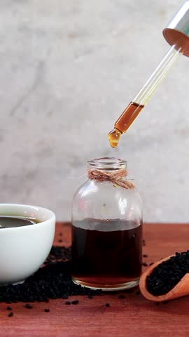 Black Seed Oil Dropping in Drops from Bottle into Glass Container