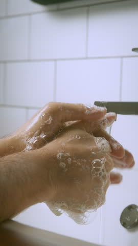 Close-up shot of hands washing under running water from a modern faucet, promoting hygiene, cleanliness, and personal care in a tiled bathroom setting – vertical stock video