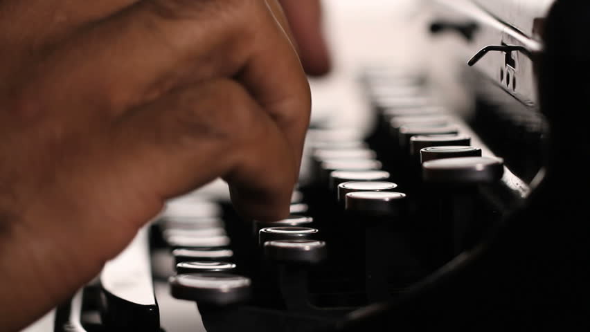 Fingers visible touch-typing on a manual typewriter. Strong backlighting.