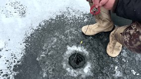 Ice fishing on frozen lake. Catching fish through an opening in the ice on a frozen body of water. Catching fish in a hole in the ice on frozen river. Winter fishing. Jigging with Small jigging rod.  - Powered by Shutterstock - Get 15% off with code: PIKWIZARD15