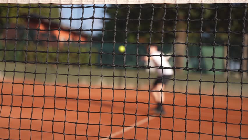 A defocused blurres young tennsi player playing tennis on a clay court and hit the ball against the net.