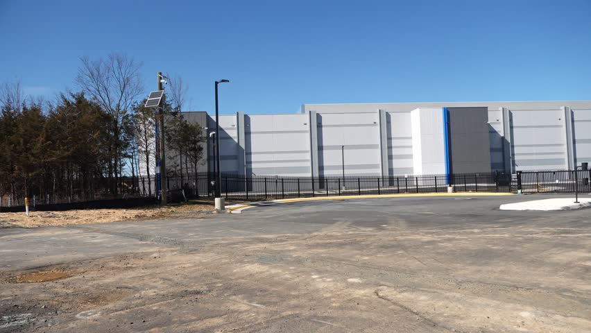 A left to right panning shot of a data center building under contruction nearing completion. A gate and fence can be seen.