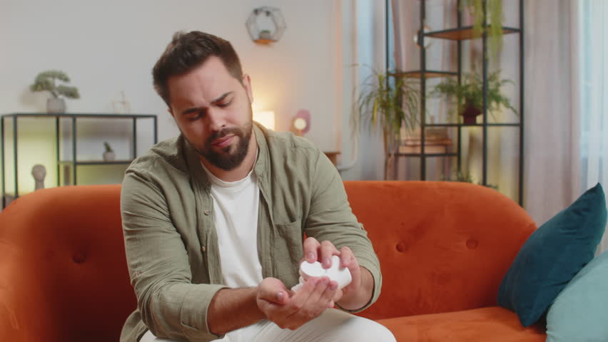 Man suffering from headache taking pill with water, wellness and treatment in living room, care and relief. Male guy with medication, anxiety or illness with aqua, medicine or cure for sickness.