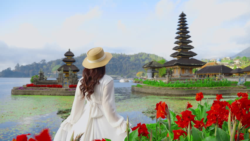 Bali, Indonesia of A female tourist wearing a straw hat walking admiring the breathtaking scenery of Ulun Danu Beratan Temple in Bali in the early morning Sunrise. Bali, Indonesia